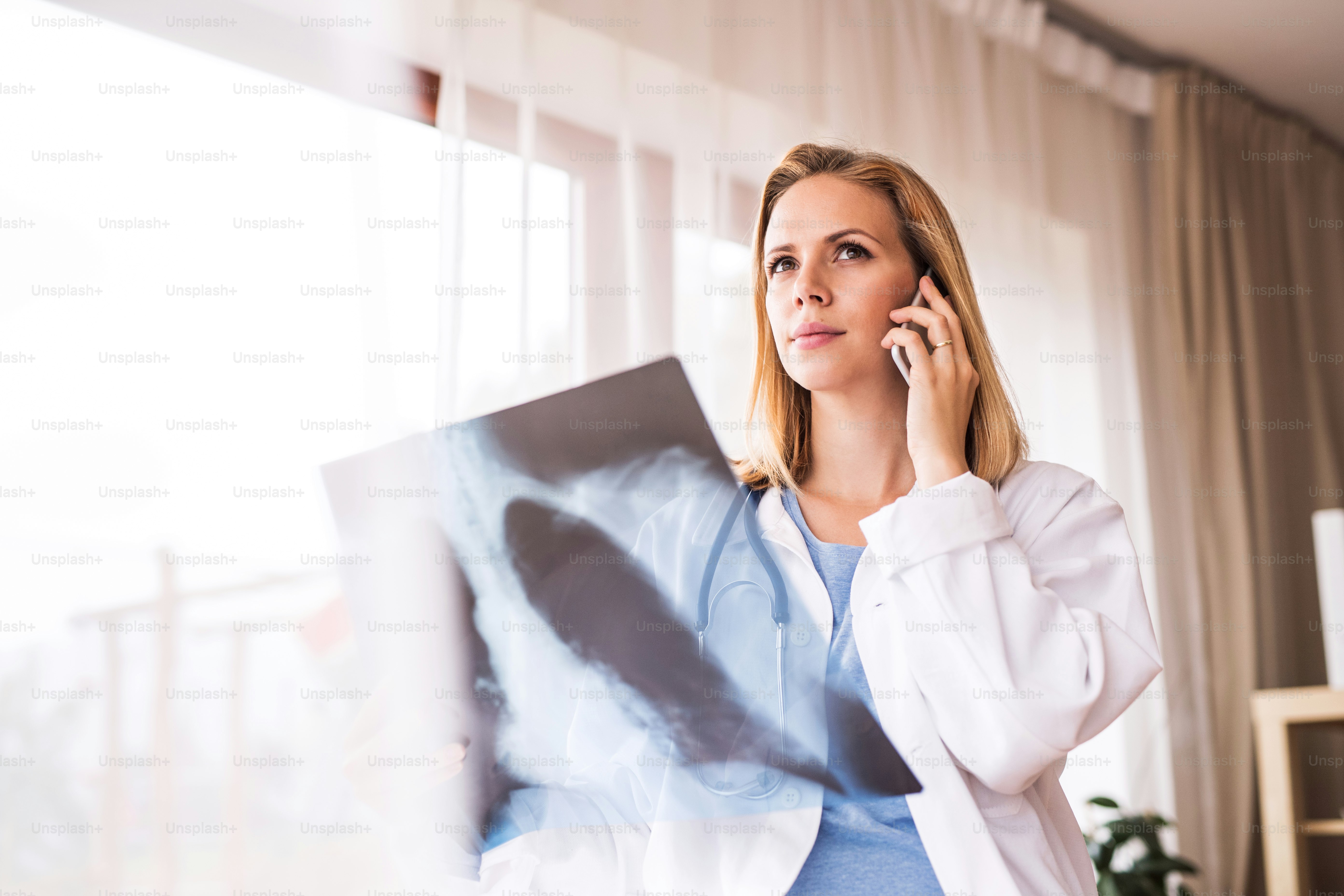 Young female doctor with smartphone at the office desk. Doctor examining an x-ray