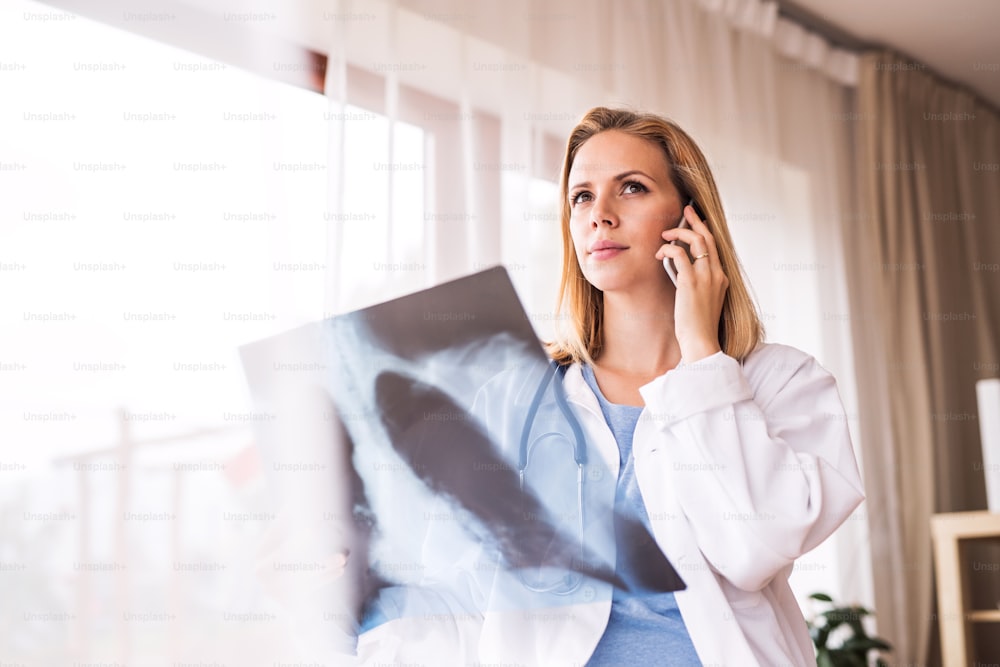 Young female doctor with smartphone at the office desk. Doctor examining an x-ray.