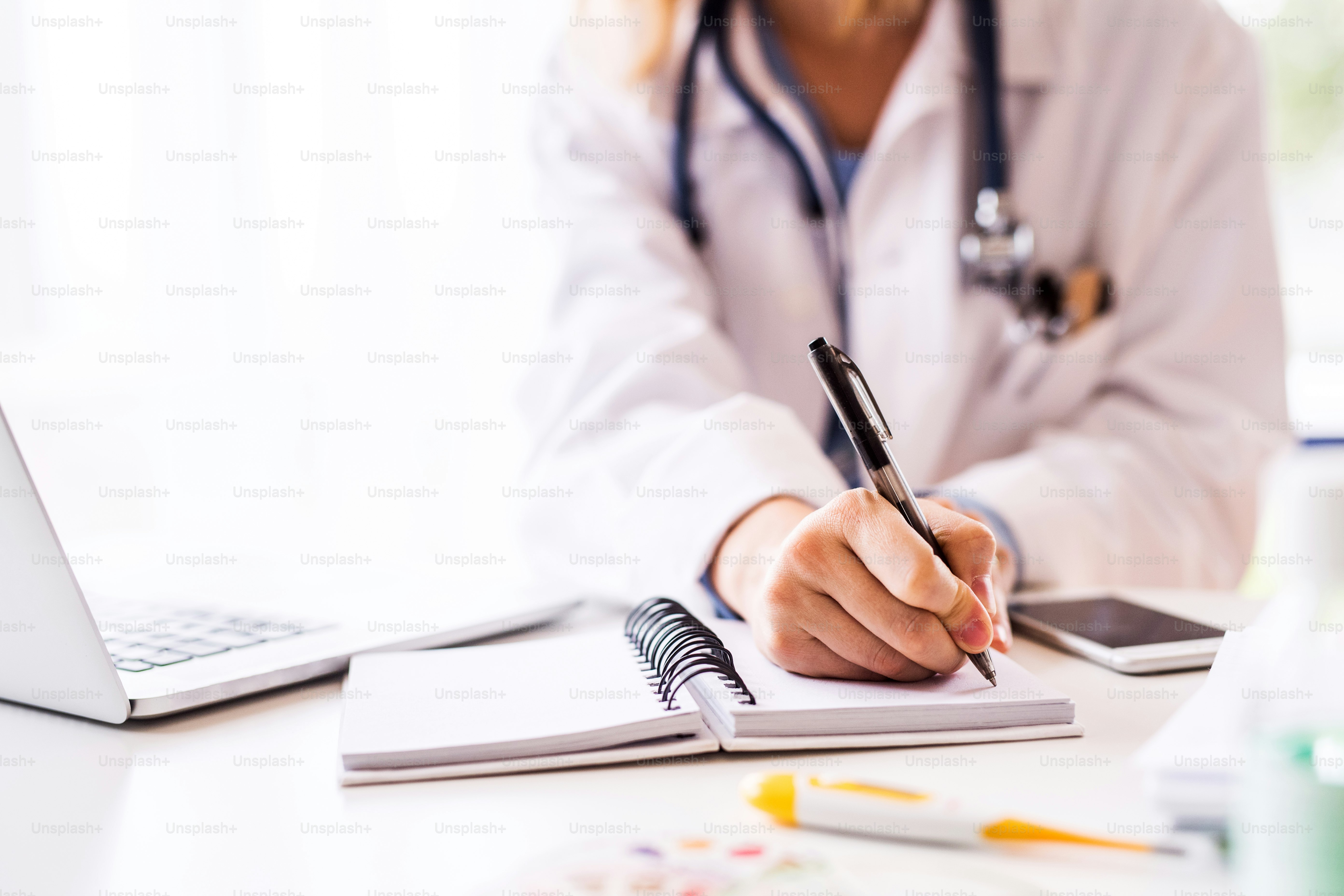 Unrecognizable female doctor working on laptop at the office desk.