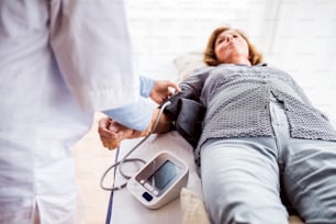 Médico irreconocible o una enfermera que controla la presión arterial de una mujer mayor en una oficina.