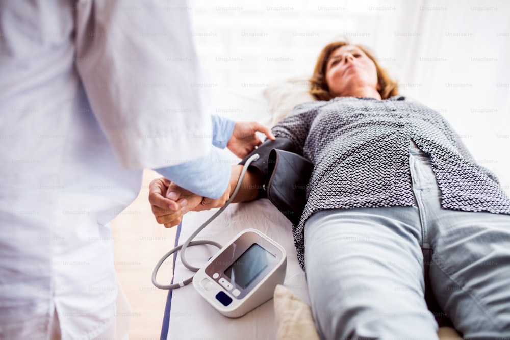 Médico irreconhecível ou uma enfermeira verificando a pressão arterial de uma mulher idosa em um consultório.