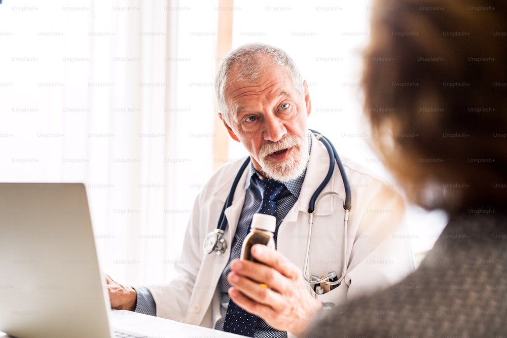 Médico con computadora portátil hablando con una mujer mayor en su oficina.