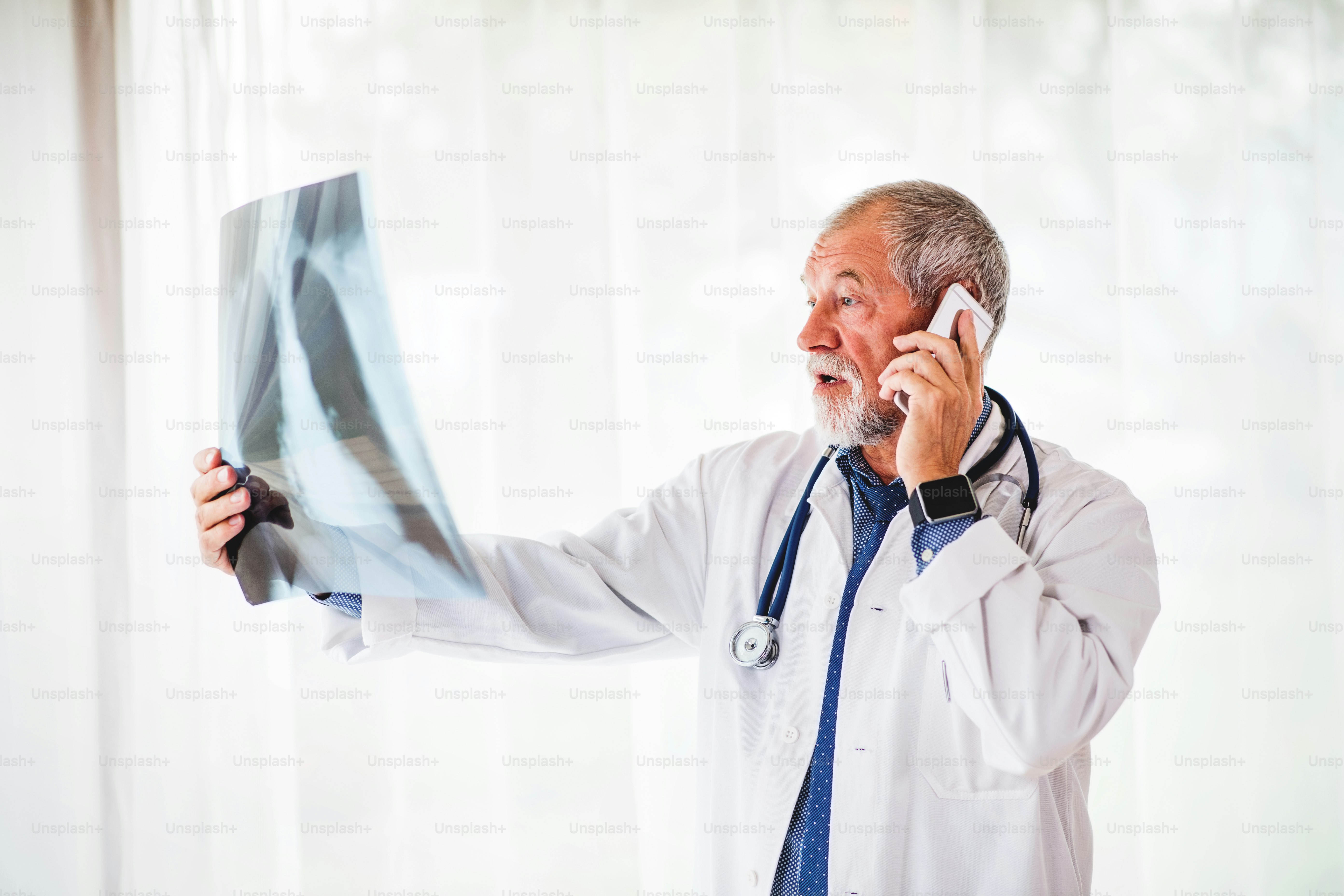 Médico senior con teléfono inteligente mirando la radiografía de tórax en su oficina. Médico masculino examinando una radiografía, hablando por teléfono.
