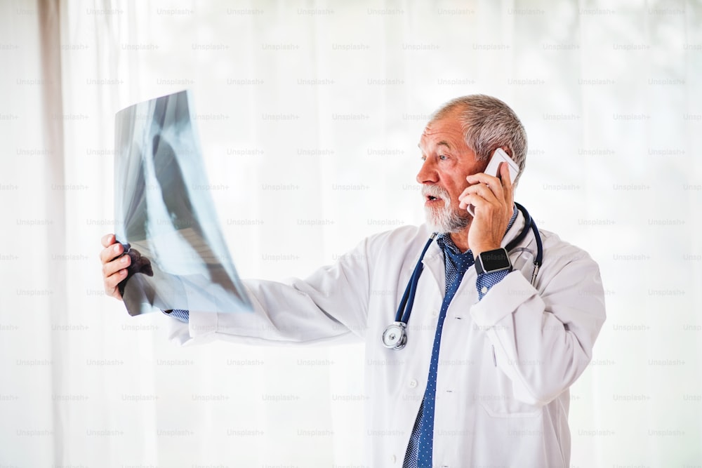 オフィスで胸部X線を見るスマートフォンを持つ上級医師。X線検査をし、電話で話す男性医師。