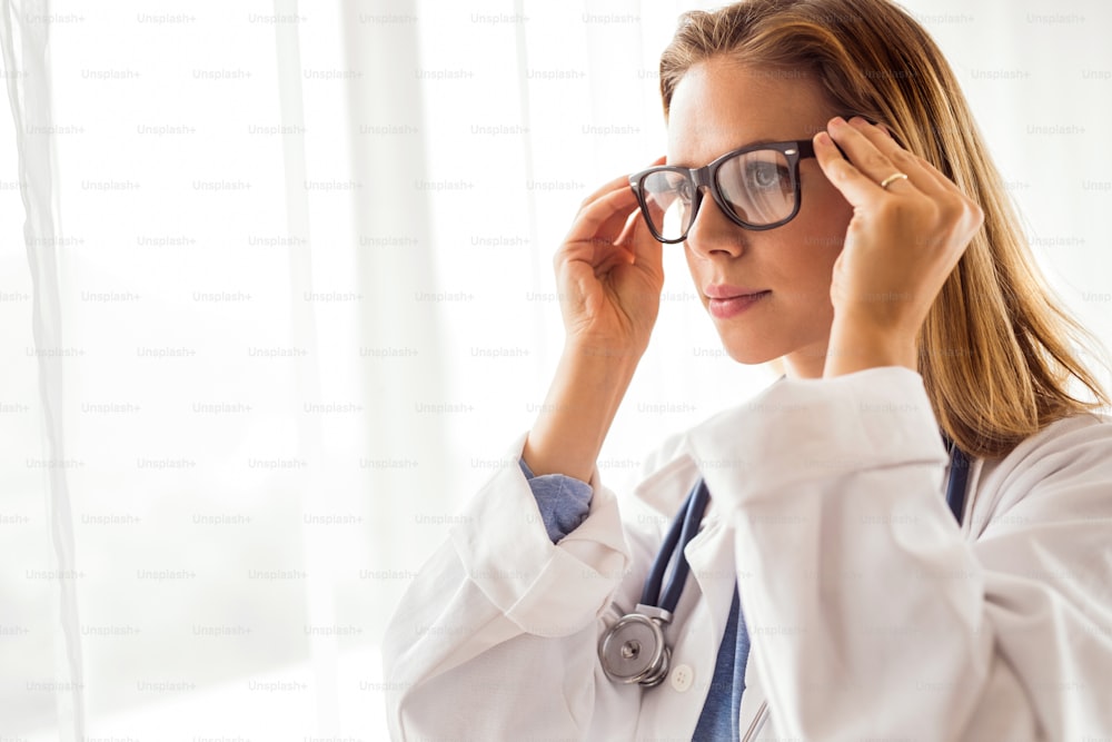 Portrait of a young female doctor putting on glasses.