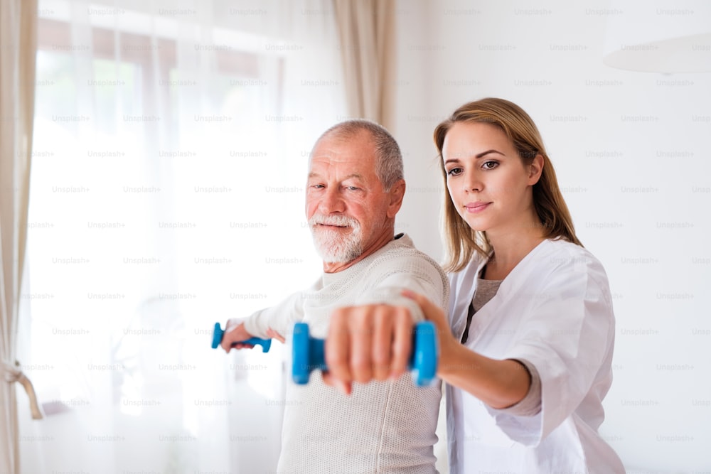 Visiteur de santé et un homme âgé lors d’une visite à domicile. Une infirmière ou un physiothérapeute aidant un homme âgé à faire de l’exercice avec des haltères.