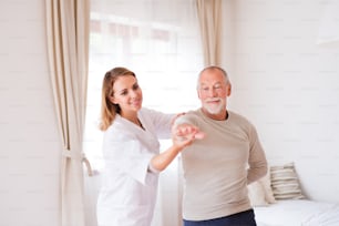 Health visitor and a senior man during home visit. A nurse or a physiotherapist helping a senior man exercise.