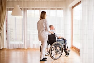 Visiteur de santé ou une infirmière et un homme âgé en fauteuil roulant lors d’une visite à domicile. Homme et femme regardant par une fenêtre.