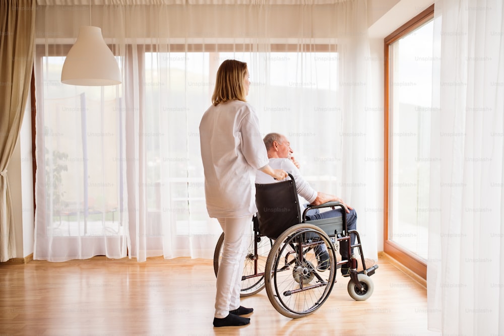 가정 방문 중 건강 방문자 또는 간호사 및 휠체어를 탄 노인. 남자와 여자가 창밖을 내다보고 있다.