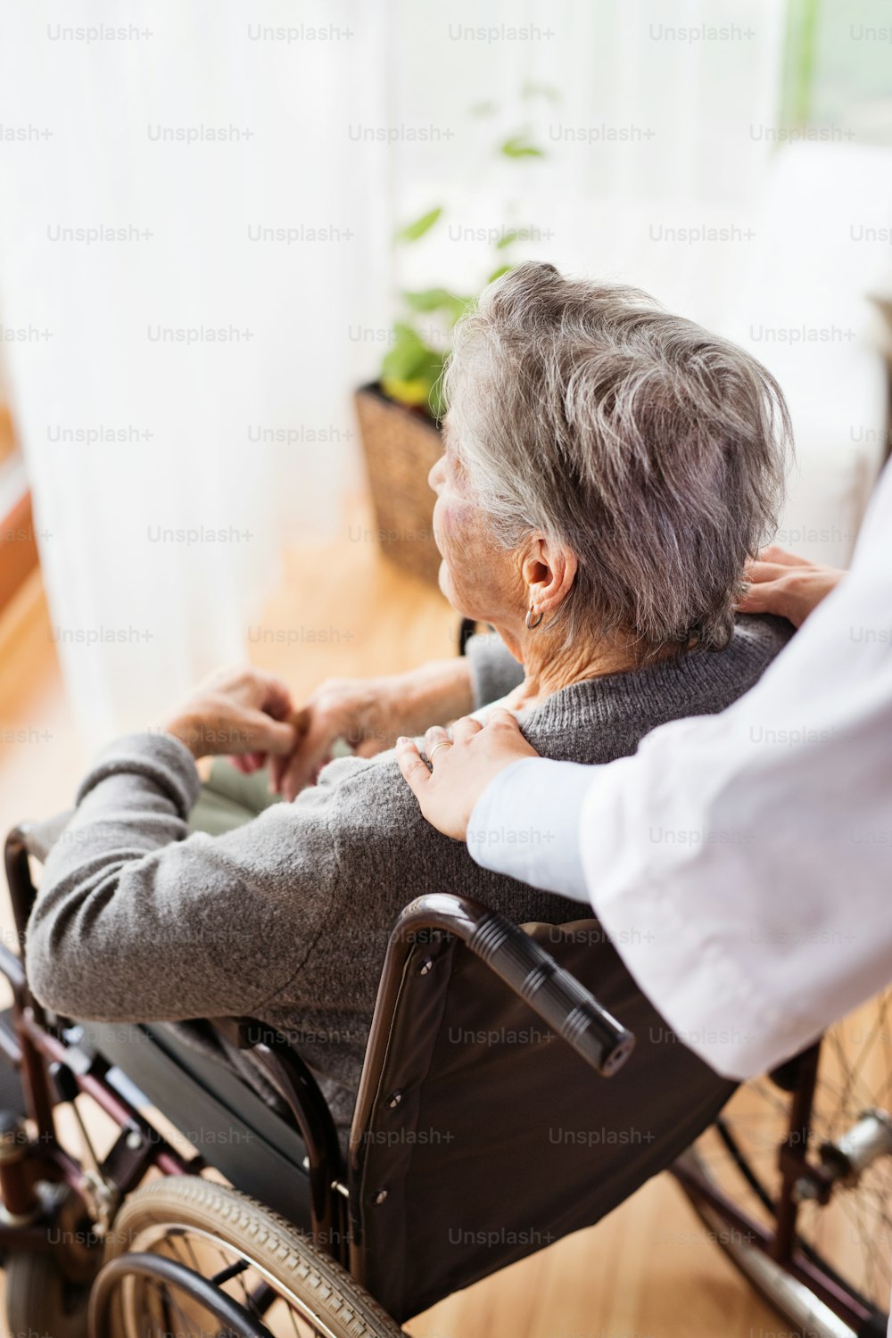 Health visitor and a senior woman during home visit. Unrecognizable nurse giving woman shoulder massage.