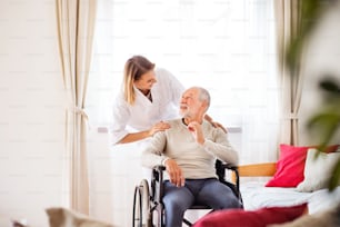 건강 방문자와 가정 방문 중 휠체어를 탄 노인. 간호사나 물리치료사가 남자와 이야기하고 있다.