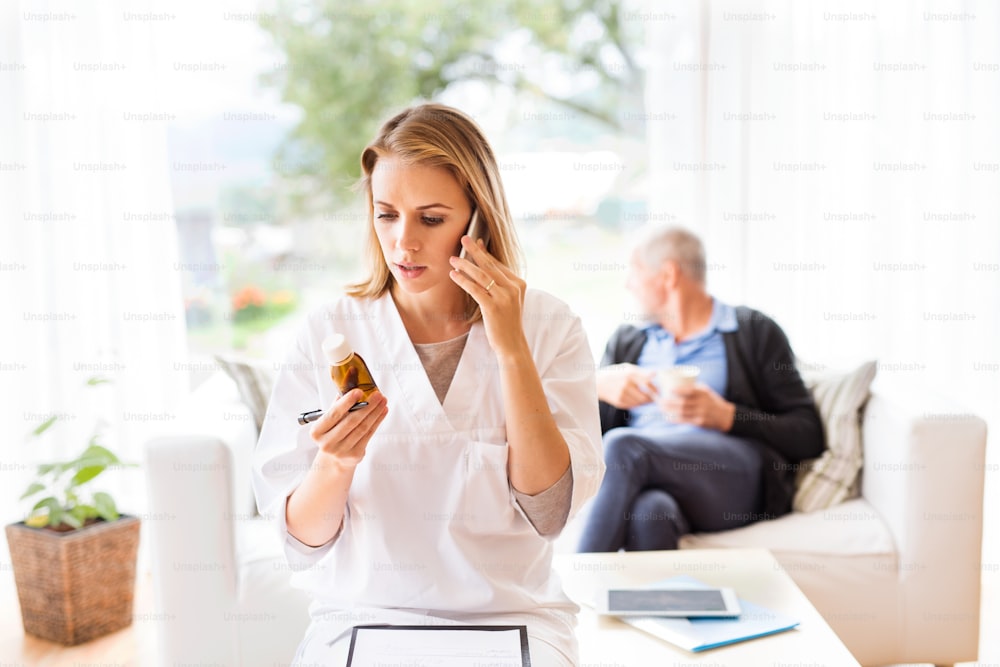 Gesundheitsbesucher mit Smartphone und ein älterer Mann beim Hausbesuch. Eine Krankenschwester oder ein Arzt, der telefoniert.