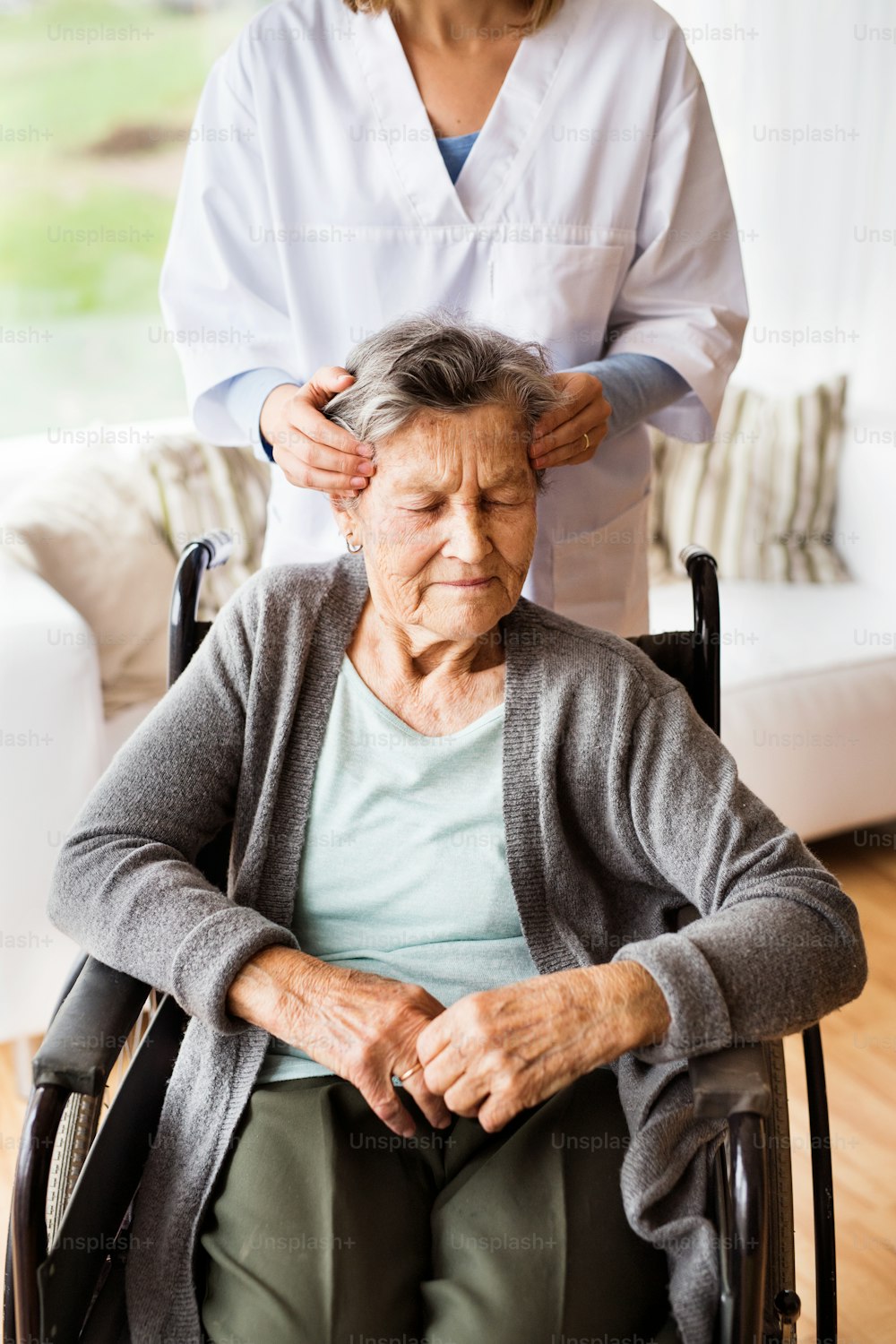 Visitador de salud y una mujer mayor durante la visita domiciliaria. Enfermera irreconocible dando masaje en el templo de la mujer.