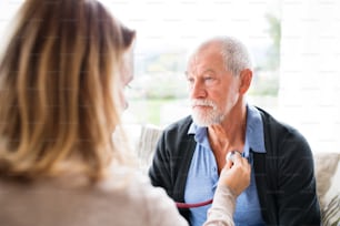 Health visitor and a senior man during home visit. A female nurse or a doctor examining a man.