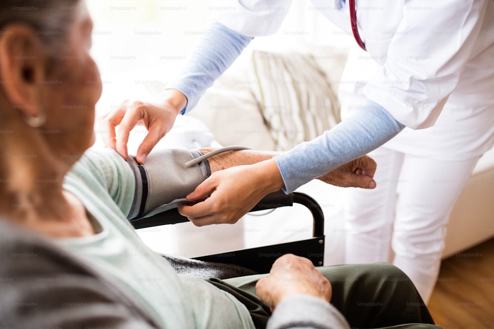 認識できない健康訪問者と家庭訪問中の年配の女性。車椅子の女性の血圧をチェックする看護師。