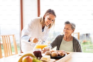 Visitador de salud y una mujer mayor durante la visita domiciliaria. Una enfermera vertiendo jugo de naranja a una anciana.