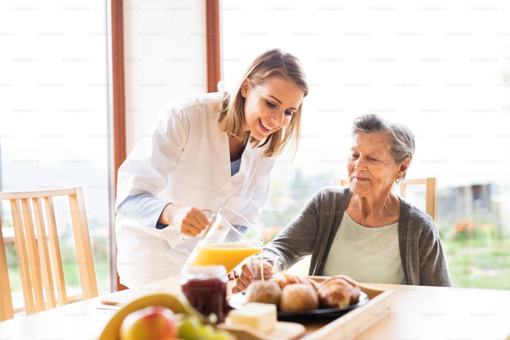 家庭訪問中の健康訪問者と年配の女性。年配の女性にオレンジジュースを注ぐ看護師。