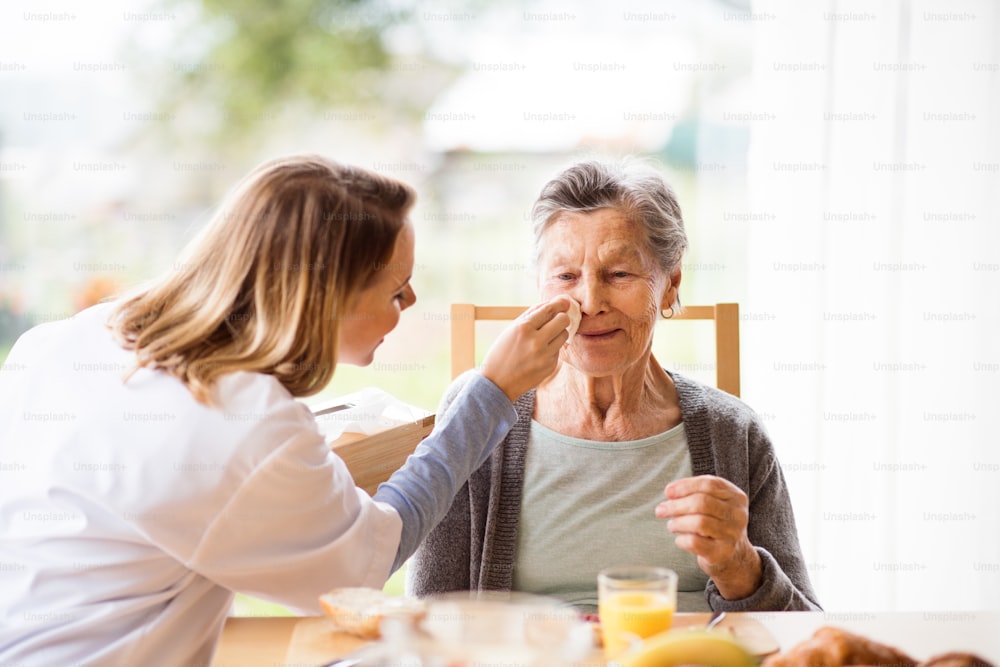 Visitador de salud y una mujer mayor durante la visita domiciliaria. Una enfermera y una anciana sentadas a la mesa.