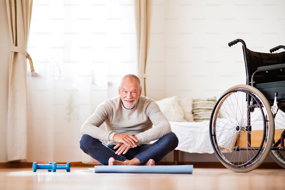 Homme âgé actif faisant de l’exercice à la maison. Homme à côté d’un fauteuil roulant.