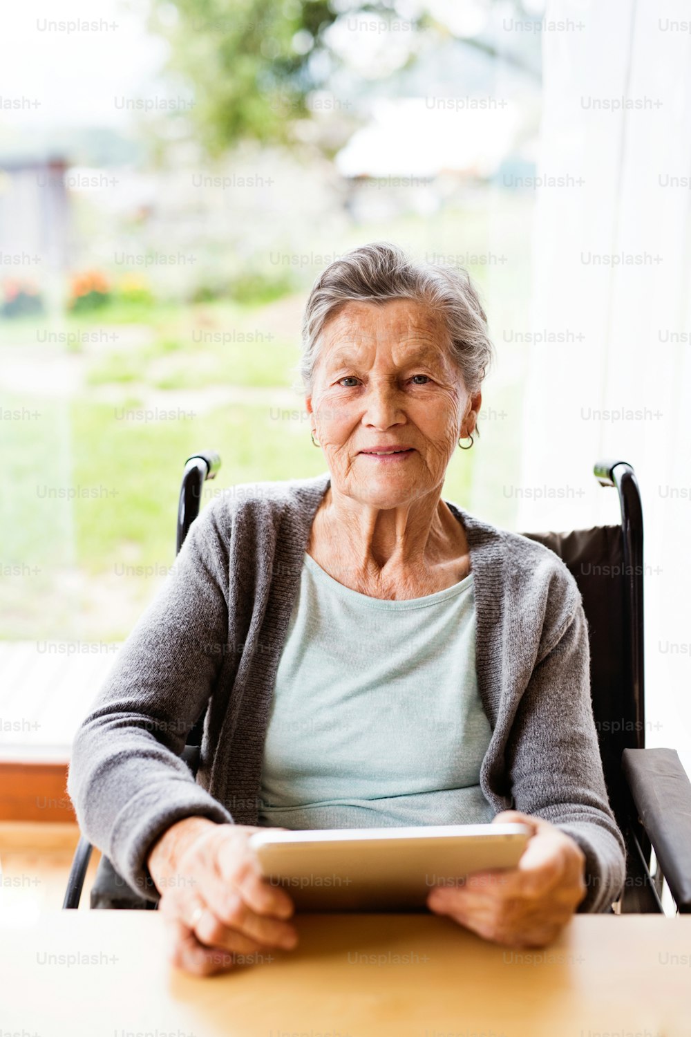 Senior woman in a wheelchair with tablet at home. An elderly woman sitting at the table.