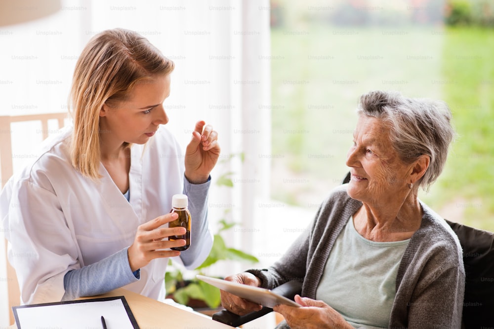 Visiteur de santé et une femme âgée avec tablette lors de la visite à domicile. Une infirmière parle à une femme âgée.