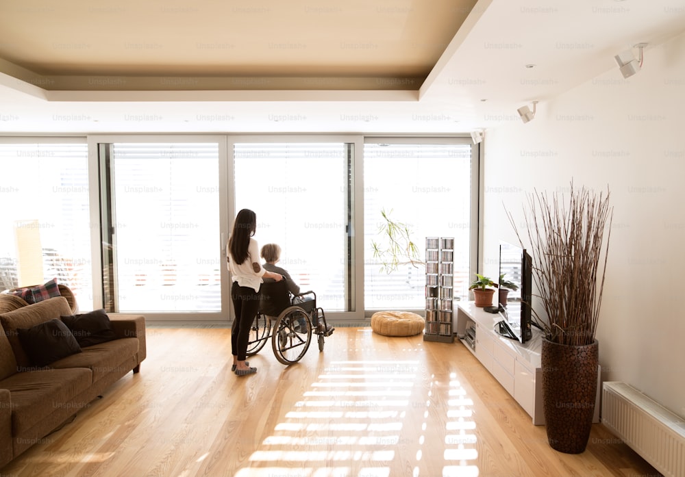 Behinderte Seniorin im Rollstuhl zu Hause in ihrem Wohnzimmer, mit ihrer kleinen Tochter, die sich um sie kümmert.