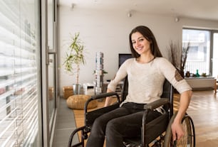 Beautiful young disabled woman in wheelchair at the window at home in her living room