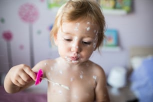 Kleines zweijähriges Mädchen zu Hause, das an Windpocken erkrankt ist, weiße antiseptische Creme, die auf den Hautausschlag aufgetragen wird. Mit Seifenblasengebläse spielen, Seifenblasen blasen.