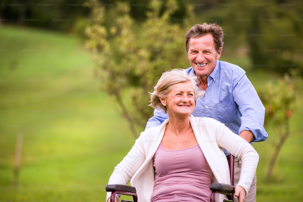Älterer Mann schiebt Frau, die im Rollstuhl sitzt, verdrängt in grüner Herbstnatur, lacht, rennt