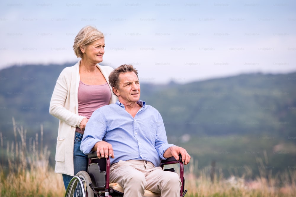 Senior woman pushing man sitting in wheelchair oustide in green autumn nature