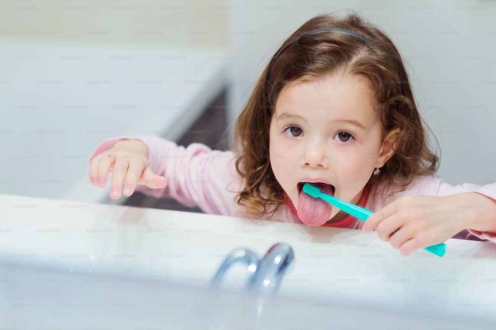 Bambina sveglia in pigiama rosa in bagno che lava i suoi denti