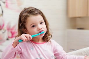 Linda niña en pijama rosa en el baño cepillándose los dientes