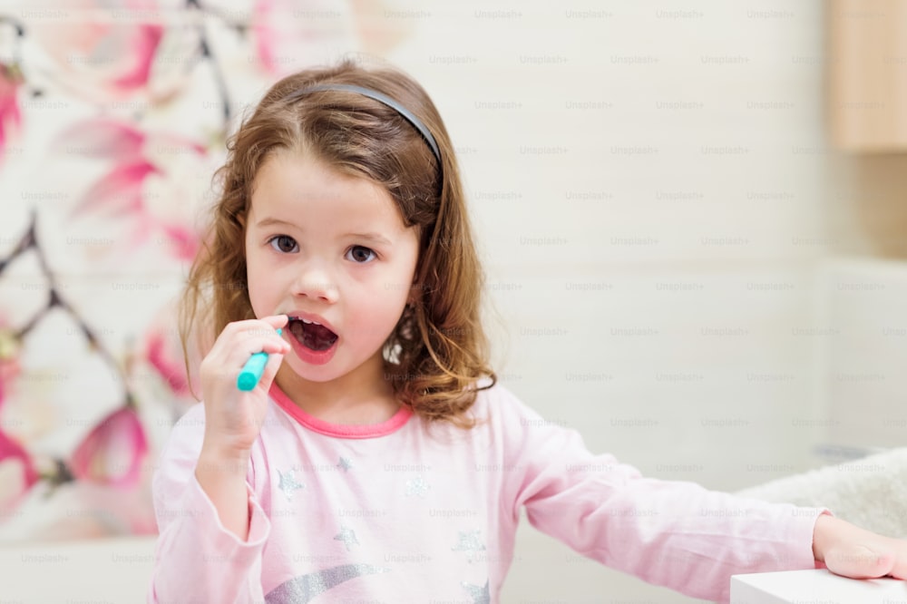 Cute little girl in pink pyjamas in bathroom brushing her teeth