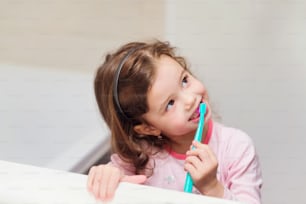 Linda niña en pijama rosa en el baño cepillándose los dientes