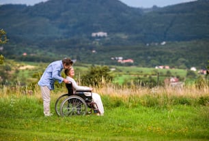 Senior man pushing woman sitting in wheelchair, kissing her, oustide in green autumn nature