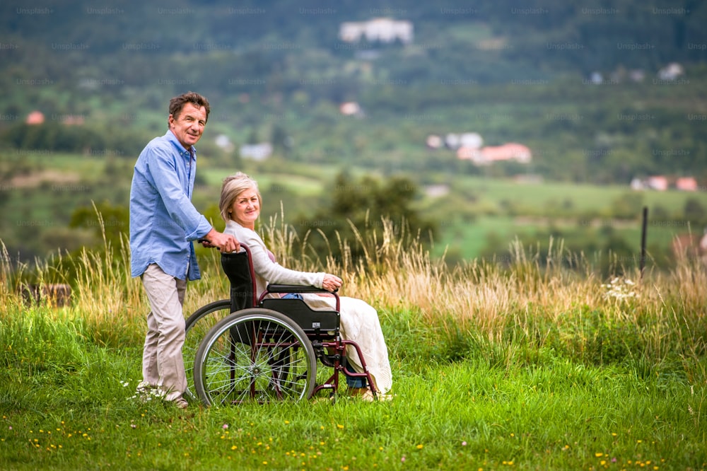 Hombre mayor empujando a una mujer sentada en silla de ruedas en la verde naturaleza otoñal