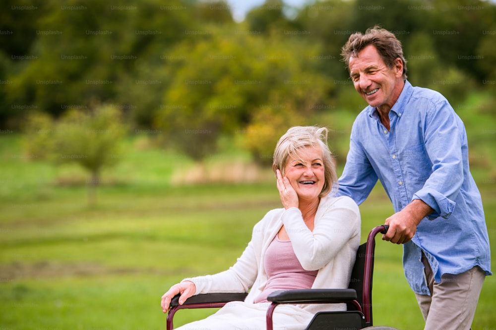 Senior man pushing woman sitting in wheelchair oustide in green autumn nature