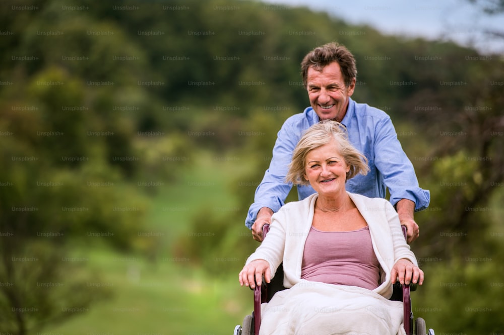 Hombre mayor empujando a una mujer sentada en silla de ruedas en la verde naturaleza otoñal