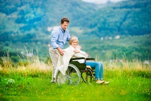 Senior man with woman in wheelchair outside in nature