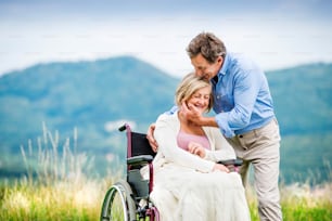 Homme âgé avec femme en fauteuil roulant à l’extérieur dans la nature