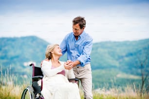 Homem sênior com mulher na cadeira de rodas fora na natureza