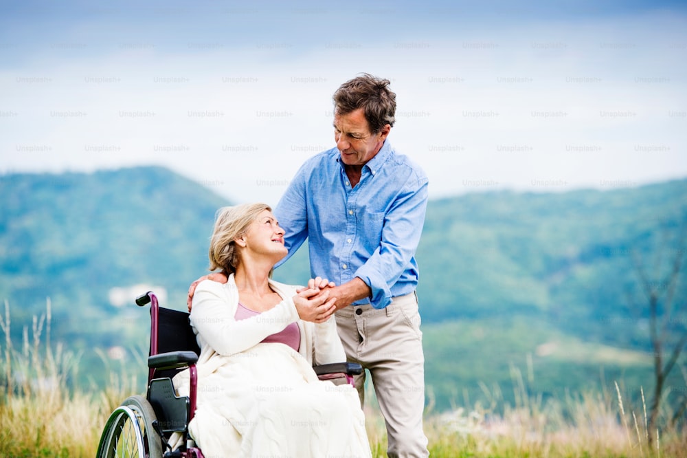 Älterer Mann mit Frau im Rollstuhl draußen in der Natur