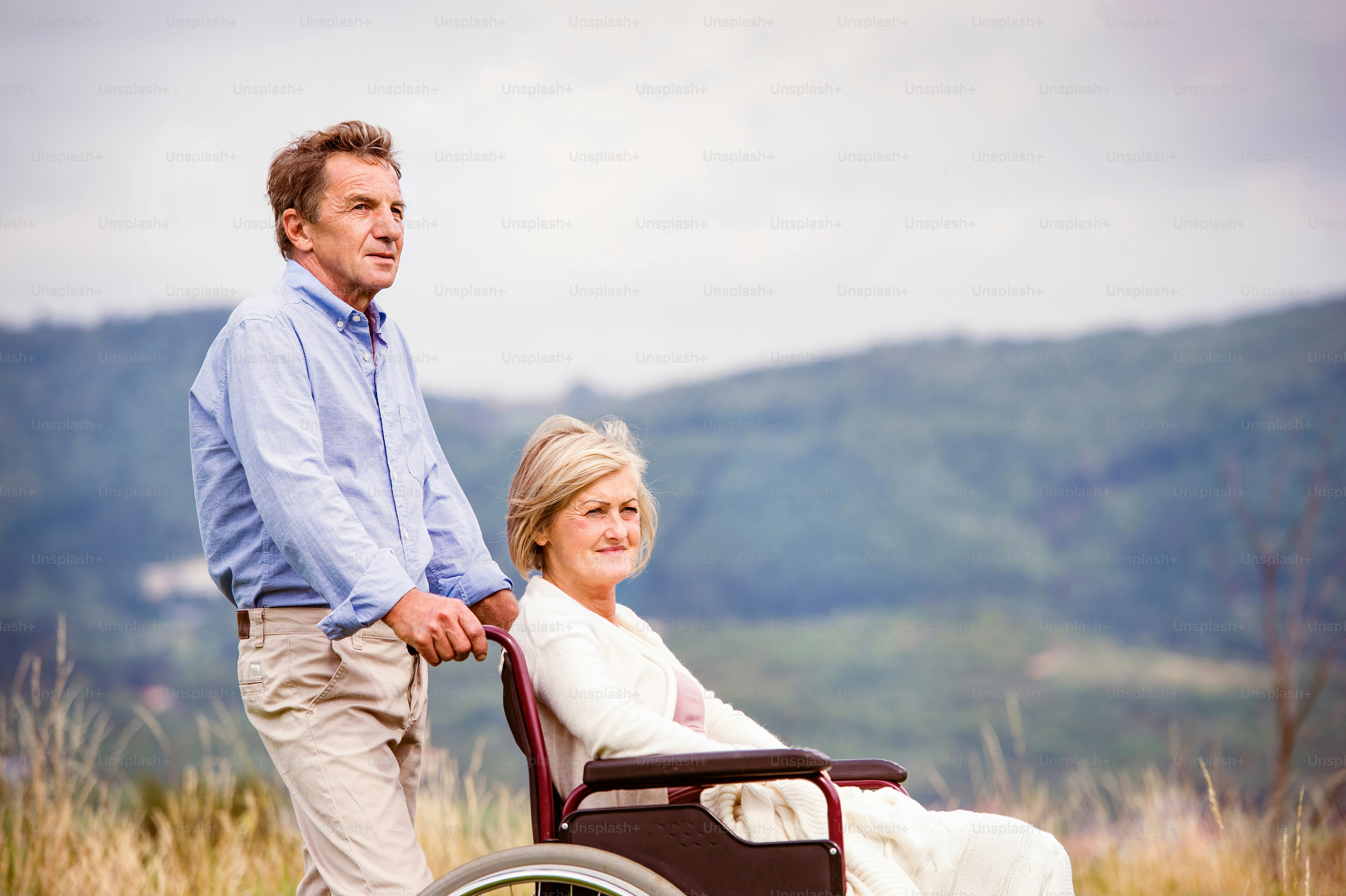 Älterer Mann mit Frau im Rollstuhl draußen in der Natur