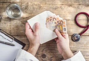 Hands of unrecognizable doctor accepting a bribe. Wooden desk background.