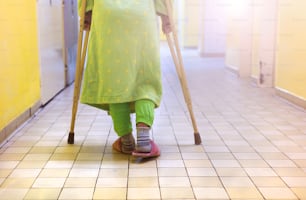 Ältere Frau verletzt, die auf dem Flur des Krankenhauses sitzt und Krücken hält
