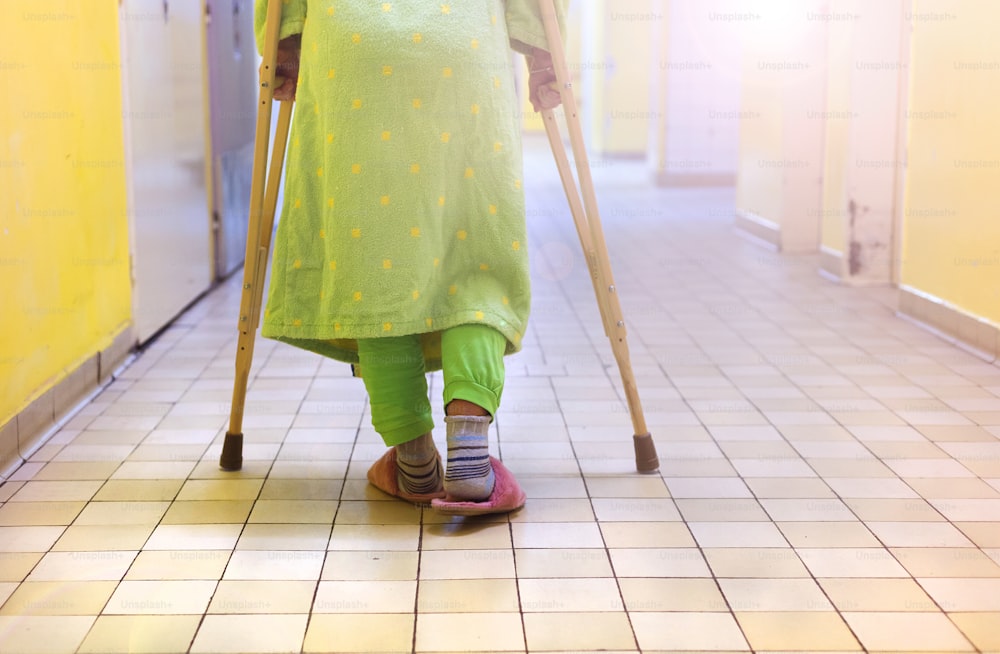Senior woman injured sitting in the hallway of hospital holding crutches