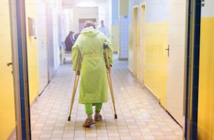 Ältere Frau verletzt, die auf dem Flur des Krankenhauses sitzt und Krücken hält