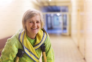 Senior woman injured sitting in the hallway of hospital holding crutches