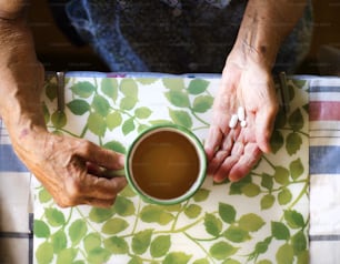 Gros plan des mains d’une vieille femme tenant des pilules dans la cuisine