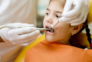 小さな女の子は歯科医に歯をチェックされています